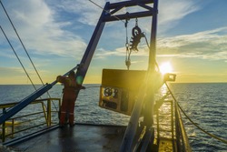  worker recovering robotics Remote Operated Vehicle (ROV) after entering sea surface during oil and gas pipeline inspection in the middle of South China Sea isolated on sunrise with glare