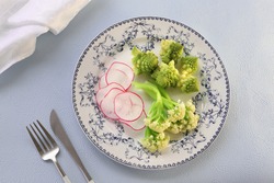 Salad plate with boiled broccoli, cauliflower and radish on pale blue background
Top view, flat lay