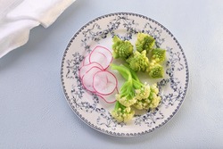 Salad plate with boiled broccoli, cauliflower and radish on pale blue background
Top view, flat lay