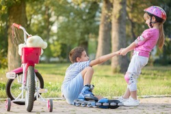 girl in park, helps boy with roller skates to stand up 
