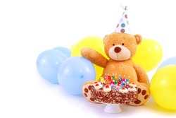 Teddy bear with birthday cap, balloons and cake with candles. Birthday greeting card, isolated, with copy space. Happy birthday cake with burning candles.