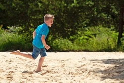 BOY RUNNING BAREFOOT AND ENJOYING MOVEMENT IN THE SAND AT THE FOREST SIDE WHILE SUN SHINING DURING SUMMER DAY