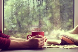 red mug of hot drink, when behind a window is rain / cozy home atmosphere