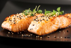 Grilled salmon, sesame seeds  and marjoram on a black plate. Studio shot