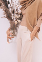 Stylish Lady in beige outfit with flowers decor.  Details of everyday look. Trendy minimalistic style. Beige aesthetics. Fashion look book. Warm Fall Winter seasons concept