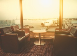 Departure lounge at the airport with seating and table with aircraft preparing for flight in the background