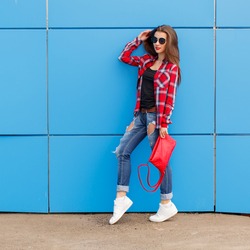 Fashion hipster girl pose in sunglasses with red bag on the blue wall. Outdoor