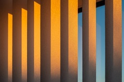 Hanging white textured vertical window slats reflecting the gold of a sunset. 