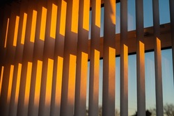 Hanging white textured vertical window slats reflecting the gold of a sunset.