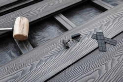 Rubber head mallet and black plastic fixings on a grey decking boards. Composite decking board installation. 