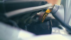 Pouring fresh new clean synthetic oil into car's engine, closeup. Shallow DOF.