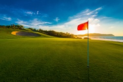 Red flag at the beautiful golf course at the ocean side at sunset, sunrise time.