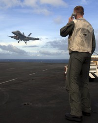 A Landing Signal Officer guides an F-18 Super Hornet aboard an aircraft carrier