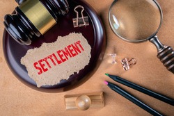 SETTLEMENT. Laws, litigation, lawyers and compromise concept. Wooden court hammer and magnifying glass on the table