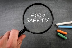 Food Safety. Colored pieces of chalk and a magnifying glass on a dark chalkboard.