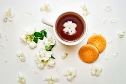 Tea cup with green tea, fragrant Jasmine flowers and biscuits in the white background. Top view composition.