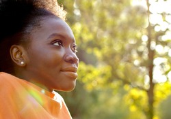Black young girl, profile face of pretty teenager smiling, with sun lights and sun spots, copy space 