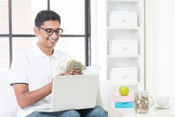 Indian guy counting cash, earning money from his successful online business. Asian man working from home.