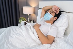 sick man in medical mask is headache and suffering from virus disease and fever in bed, coronavirus (covid-19) pandemic concept.