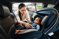 happy mother is fastening safety belt to newborn baby in the car seat