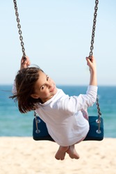 Little girl swinging with the sea in the background