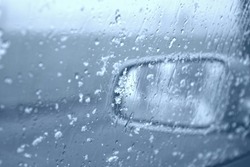Droplets and snowflakes on car window and rear view mirror