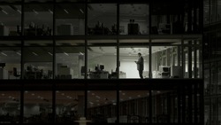 Man working late night in empty building with transparent glass window, modern