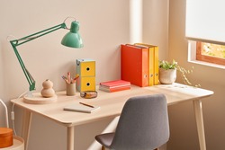 Chair placed near table with lamp and colorful stationery in cozy home office in morning
