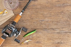 Fishing rod cork handle with reel and plastic fish bait lures have sharp metal hoop pace on old wood table for background, Vintage wood and fishing equipment, Holiday travel to fishing are hobbies.