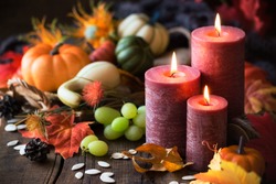 Thanksgiving dinner concept. Lit candles with pumpkins, grapes, autumn leaves and fall decorations 