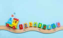 Toys background with copy space. Kids toy train with numbers on toy wooden railway on light blue background with blank space for text. Top view, flat lay.