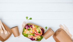 Healthy food in disposable eco friendly food packaging. Vegetable salad in the brown kraft paper food containers on white wooden background with blank space for text. Top view, flat lay.