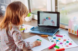 Beautiful toddler girl molding colorful clay cloud with rain watching online learning lesson on the laptop indoor. Distance home learning concept.