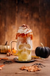 Idea for kids Halloween party table. Freak Monster shake in scull jar topping with whipped cream and caramel on wooden background. Selective focus.