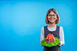 Schoolgirl holding her scientific project volcano on blue background with blank space for text