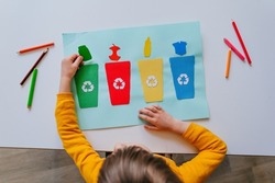 Little girl playing with poster of garbage containers for sorting at kindergarten or primary school. Recycling education concept.