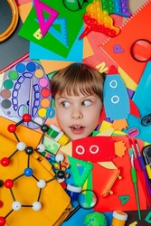 Funny girl's face with surprise emotion surrounded by different school stationery. Top view, flat lay. Back to school concept background.