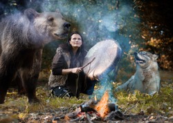 Female shaman playing her shaman sacred drum in the forest among wild animals - a dog and a bear. The theme of totem animals in shamanism