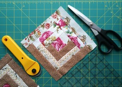  On the mat for patchwork sewing there are scissors, a knife for patchwork, a ruler, a patchwork napkin  