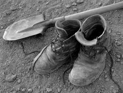pair of well worn work boots and spade on the ground
