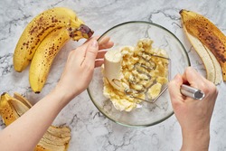 Woman hand mashing up several bananas to bake into a banana bread.