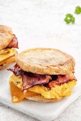 English muffin, scrumbled egg, ham, and cheese breakfast sandwich on a cutting board