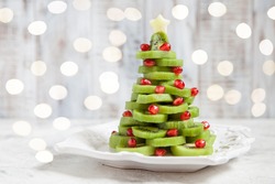 Healthy dessert idea for kids party - funny edible kiwi pomegranate Christmas tree, beautiful New Year background