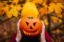  Girl holding jack-o-lantern in front of face. Carved halloween spooky pumpkin. Gold autumn colors.