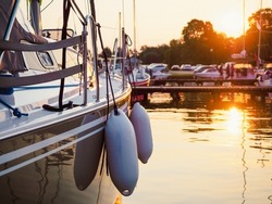sunset view on sailing yacht moored on jetty in the port, close up view on sailboat hull, bow and fenders