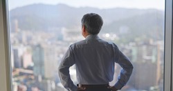 asian senior businessman is looking at city view through window