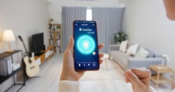 Asian young woman is using smart home app and touch screen to turn on the light by mobile phone