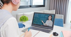 rear view of asian girl is learning math online through listening to female high school teacher teaching trigonometric function by  laptop at home and write down the note