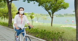 Asian female wear mask with smile and ride bicycle in the park