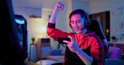 asian man have live stream and win mobile game on the smartphone with raising arm at home